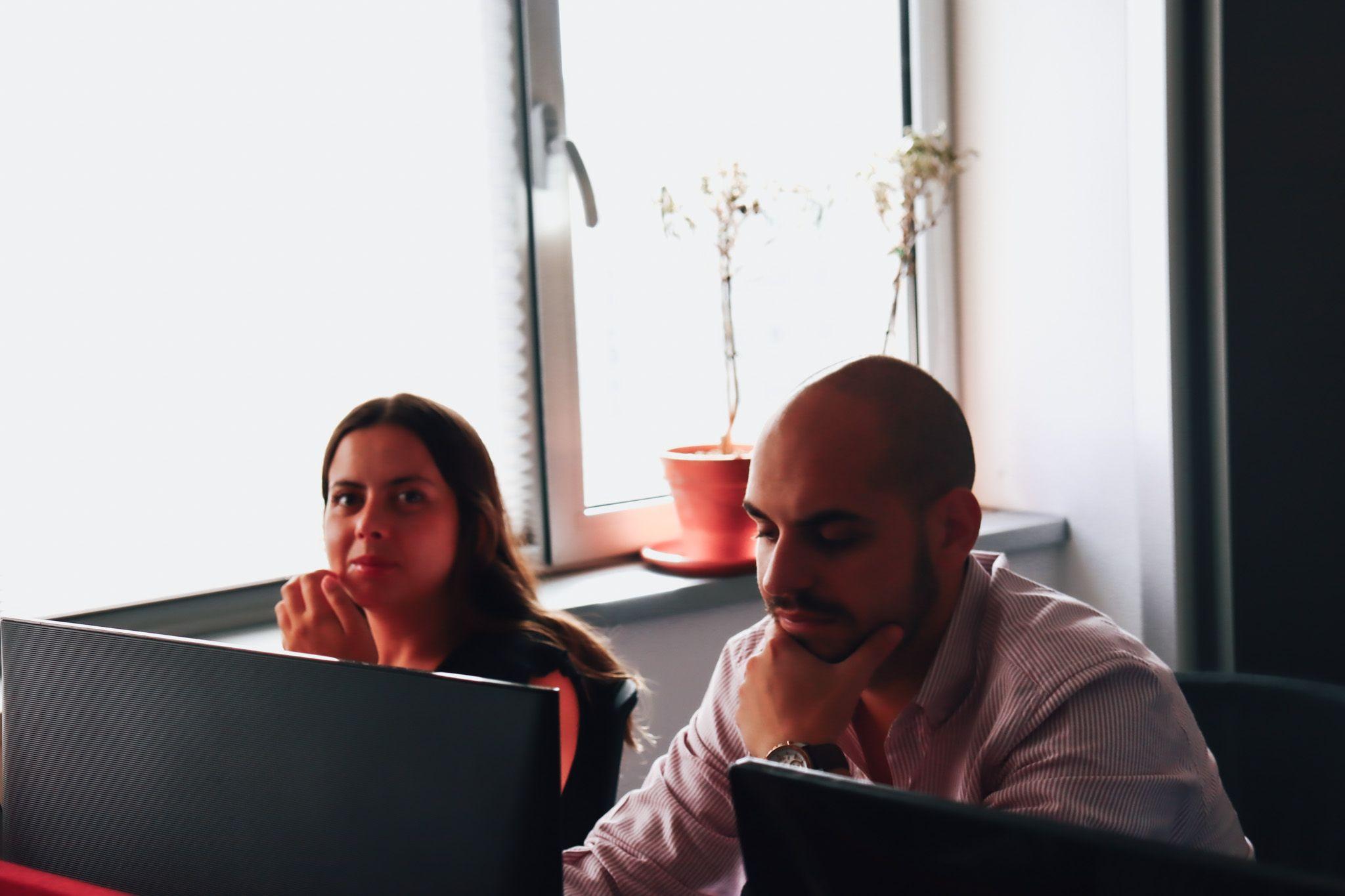 two members of the red.it team working together at the desk. Office background in red tones.