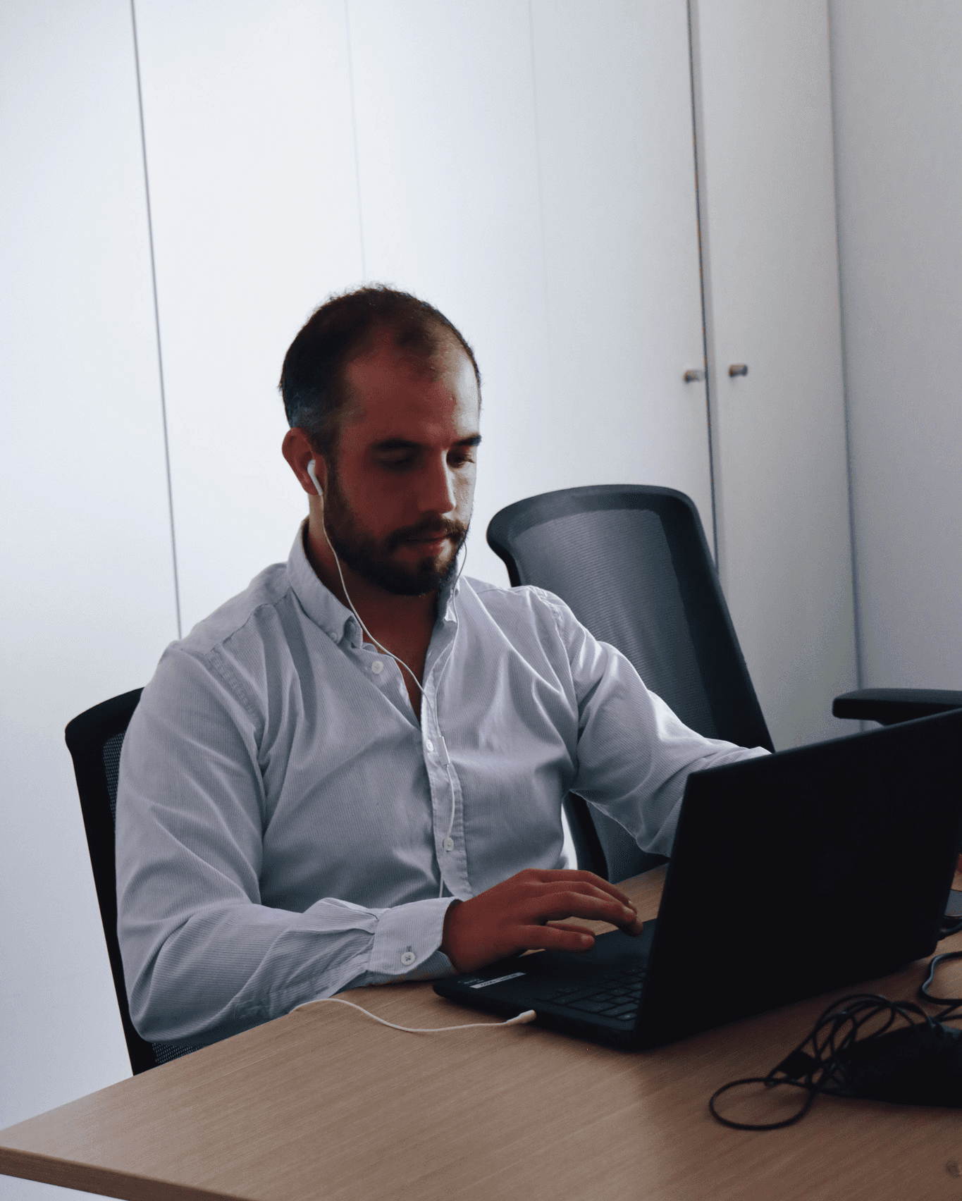 man focused and working on the computer, dressed in a baby blue shirt. In the background, a white cabinet