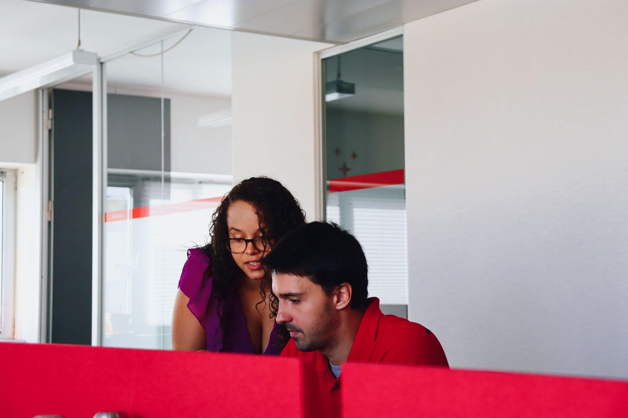 two co-workers working at the same table, focused on their computer. office background in red tones.